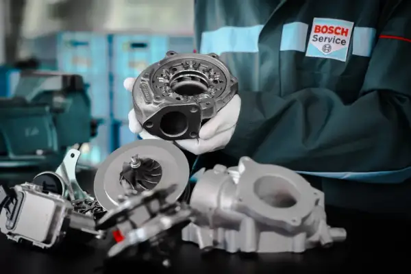 Mechanik w białych rękawiczkach prezentuje części turbosprężarki biturbo.