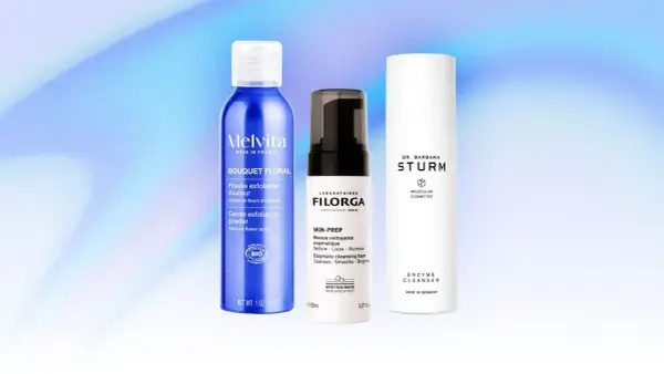 Tre flaconi di prodotti per la cura della pelle, tra cui una polvere esfoliante e due detergenti enzimatici, su sfondo blu sfumato.