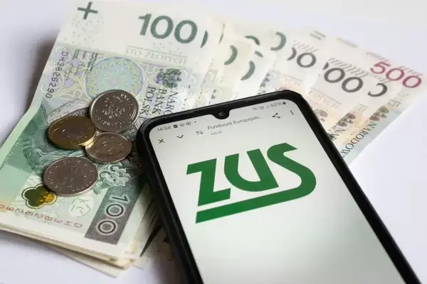Złotówki i monety na tle ekranu telefonu z logo ZUS. Sprawdź, ile jest zasiłku pogrzebowego.
