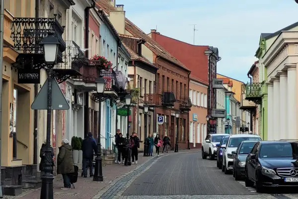 Urokliwa ulica w Koninie z kolorowymi kamieniczkami, balkonami i ludźmi spacerującymi po bruku. Odkryj **konin atrakcje** spacerując tymi uliczkami.