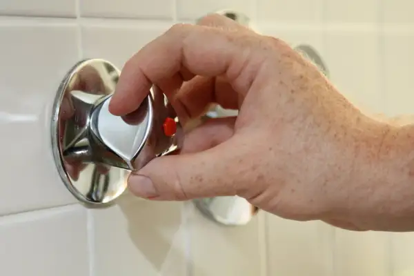 Hand dreht am Duschthermostat, um den wasseranschluss abzudichten.