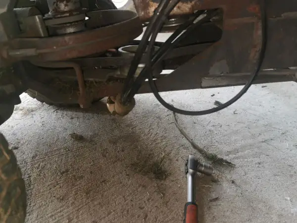 Jak założyć pasek do kosiarki traktorka Husqvarna? Widok mechanizmu napędowego z kluczem nasadowym.