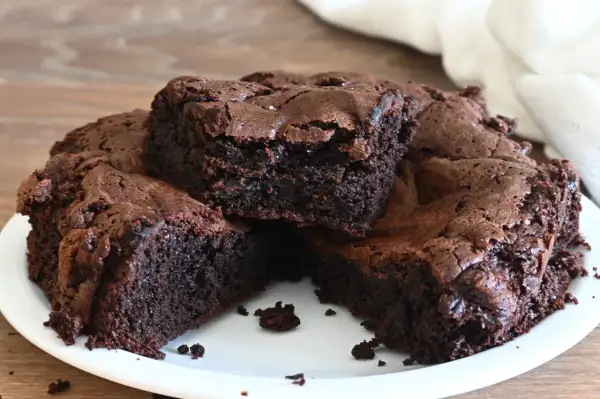 Una torta cioccolatino ricca e umida, tagliata a fette su un piatto bianco. La superficie è leggermente screpolata, con cristalli di sale visibili.