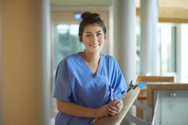 Glad ung kvinna i blå scrubs med en clipboard, redo för sin laborant utbildning.