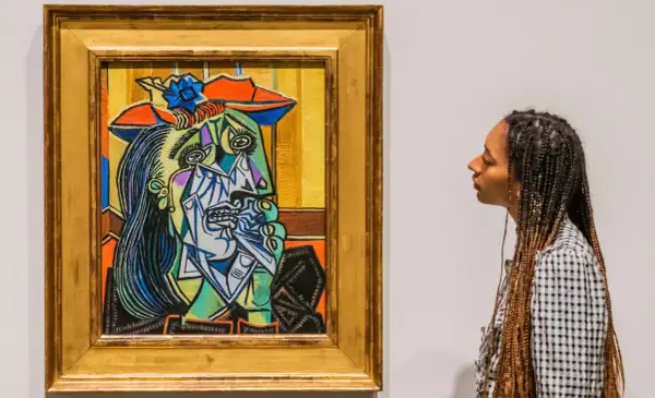 A woman gazes at a vibrant, cubist portrait, a striking example of obras de Pablo Picasso. The painting features a fragmented face with bold colors and sharp lines.