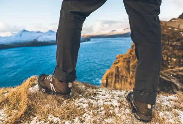 Nogi w butach trekkingowych na tle błękitnego morza i ośnieżonych gór. To prawdziwy hiking po polsku, pełen przygód i pięknych widoków.