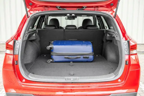 Otwarty bagażnik czerwonego Hyundai i30 kombi z niebieską walizką. Sprawdź pojemność bagażnika na podróż!