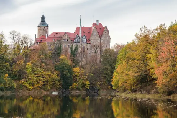 Zamek Książ w jesiennej odsłonie, idealne miejsce na jednodniowy wypad w Polsce. Otoczony kolorowymi drzewami, odbija się w spokojnej tafli wody.