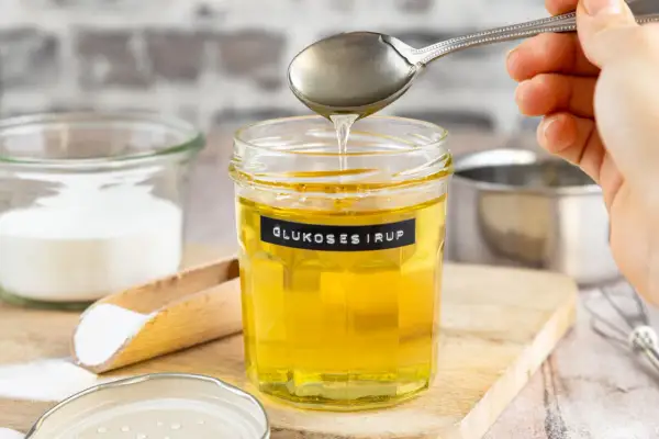 Glas mit Glukosesirup, bereit für leckere glucose rezepte. Daneben Zucker und ein Schneebesen.