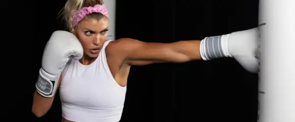 Woman in white sports bra and pink bandana throws a punch, her glove about to fade back from the impact.