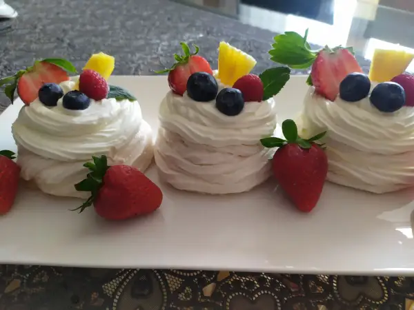 Mini bezy pavlova z bitą śmietaną, truskawkami, borówkami i ananasem.