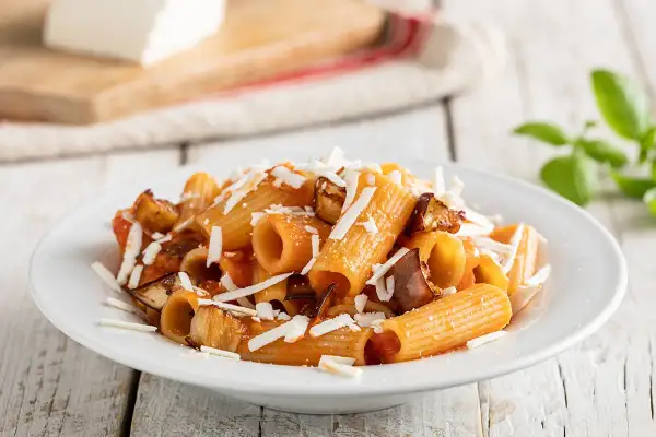 Piatto di pasta alla norma ricetta originale con melanzane fritte, pomodoro e ricotta salata grattugiata.