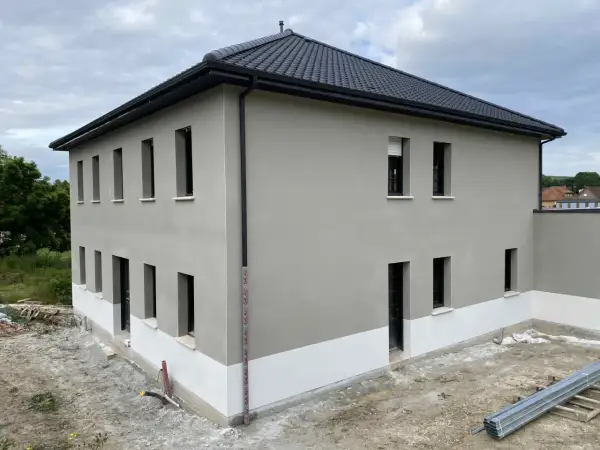 Maison neuve avec enduit de façade gris clair et soubassement blanc. Le chantier est en cours, montrant comment faire un enduit de façade.