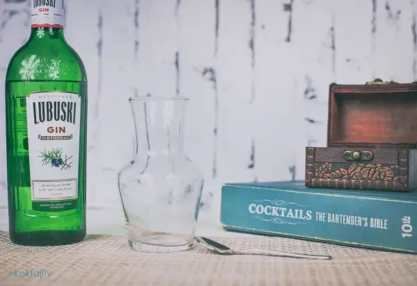 Butelka Lubuski Gin, pusta karafka, łyżka barmańska i książka "Cocktails The Bartender's Bible" sugerują przygotowanie drinków.