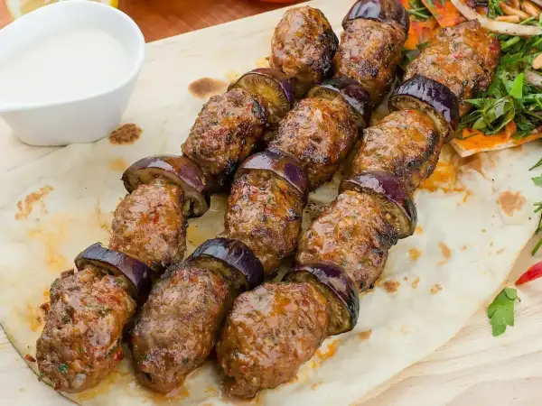 Kofta kebab z bakłażanem na patyku, podany na chlebku z sosem.
