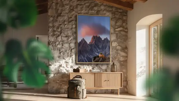 Quadro con montagne al tramonto, che cattura vibranti spazi colore. Zaino e mobile in legno completano l'arredo rustico.