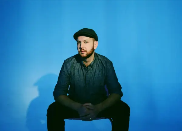 Matt Simons, nach dem Erdrutsch, sitzt nachdenklich vor blauem Hintergrund.
