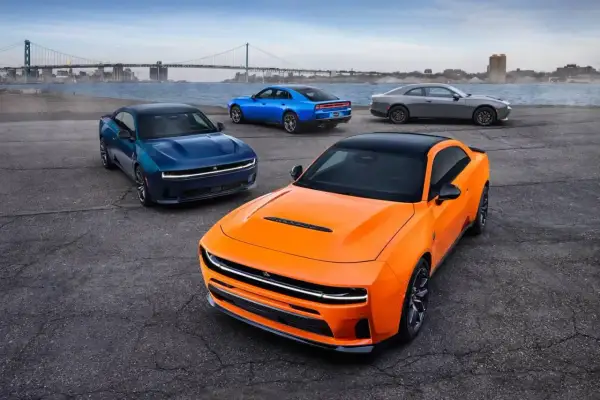 Pomarańczowy i niebieski Dodge Charger Hellcat oraz szary Charger stoją nad wodą.