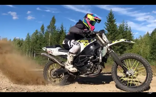 Motocyklista w kolorowym kasku pędzi na crossie, wzbijając tumany kurzu.