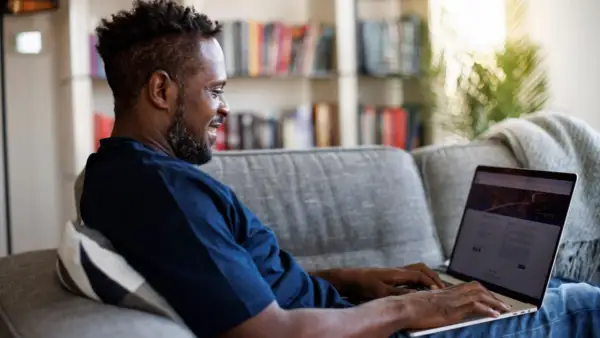 Mann auf Sofa nutzt Laptop, um mit umfragen geld verdienen steuer.