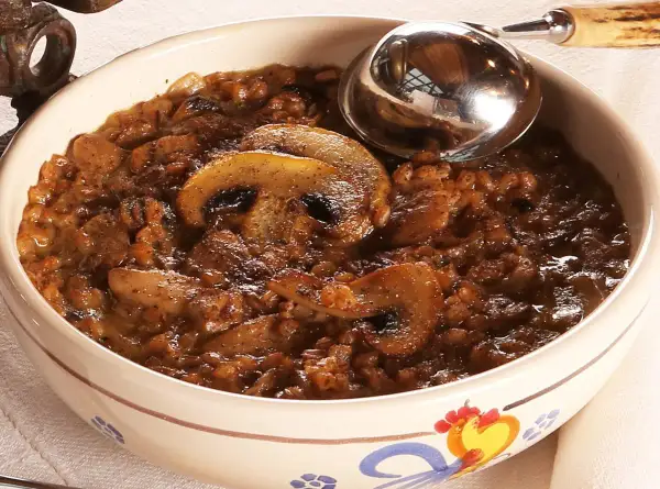 Una ciotola decorata con una ricca zuppa di farro e funghi, pronta per essere servita con un mestolo.