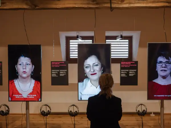 Eine Frau betrachtet drei Bildschirme mit Porträts von Frauen. Die Installation thematisiert die **Vergangenheit gegenwart** und individuelle Interviews aus Ost- und West-Berlin.