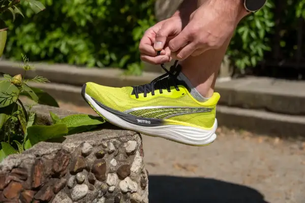 Dłoń wiąże sznurówki jaskrawożółtego buta Puma Deviate Nitro 3, gotowego na bieg.