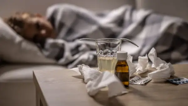 Sjuk person i sängen med medicin, glas vatten och näsdukar på bordet. Viktigt för att minska sjukfrånvaro.