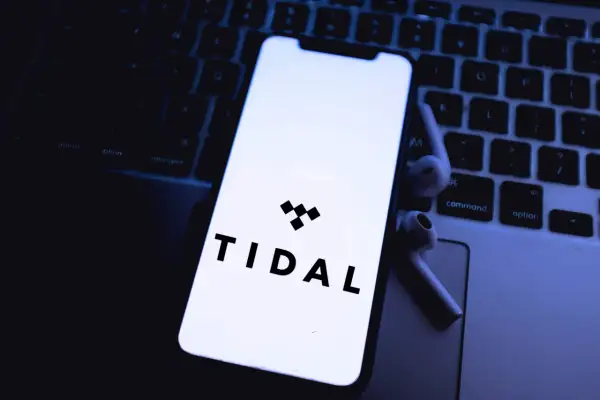 Smartfon z logo Tidal na klawiaturze laptopa i słuchawkami bezprzewodowymi.