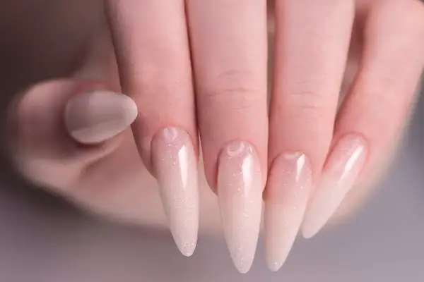 Delikatny manicure baby boomer na długich paznokciach, z subtelnym brokatem.