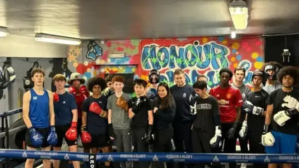 A group of young boxers, some wearing gloves, stand in a boxing ring. One boxer is in the foreground, ready to run.