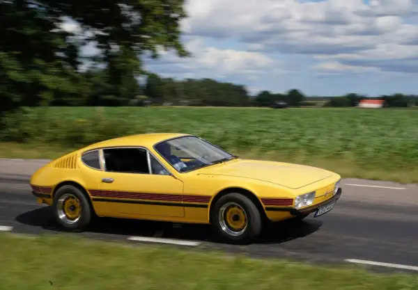 Gul vw sp2 susar fram längs en landsväg, med gröna fält och moln som suddas ut i bakgrunden.