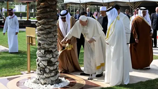 Papież Franciszek i przywódca Zjednoczonych Emiratów Arabskich wspólnie podlewają drzewo. W tle widać ludzi w tradycyjnych strojach, jakby na spotkaniu z muezinem.