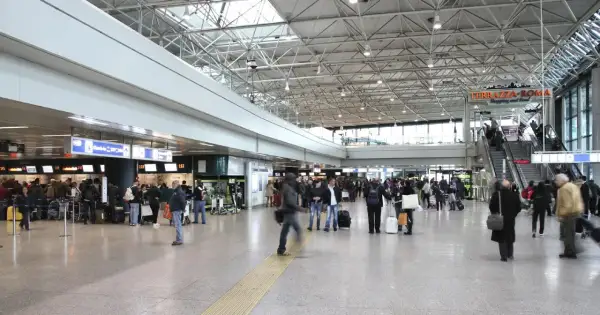 Tłoczny terminal lotniska Rome Ciampino, ludzie z bagażami czekają w kolejce do odprawy.