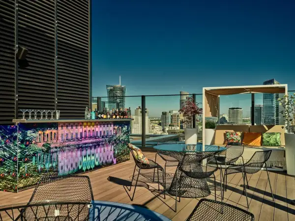 Elegancki ether rooftop bar z widokiem na miasto. Kolorowy bar, stoliki i wygodne fotele zapraszają do relaksu.