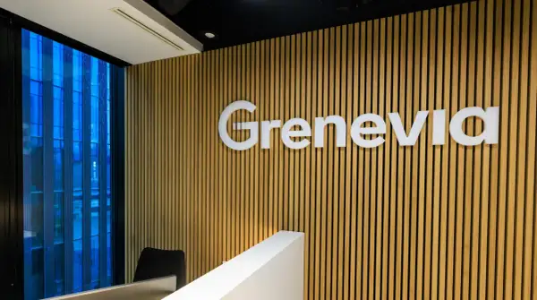 Nowoczesne biuro z logo Grenevia na drewnianej ścianie. Za oknem błękitny, deszczowy krajobraz miejski.