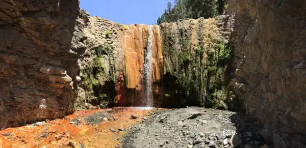 Cascada rojiza y verde en un cañón rocoso, ideal para senderismo en Palma de Mallorca.