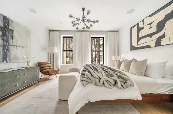A luxurious bedroom with modern decor, featuring a plush fur throw on the bed, abstract art, and a statement chandelier.