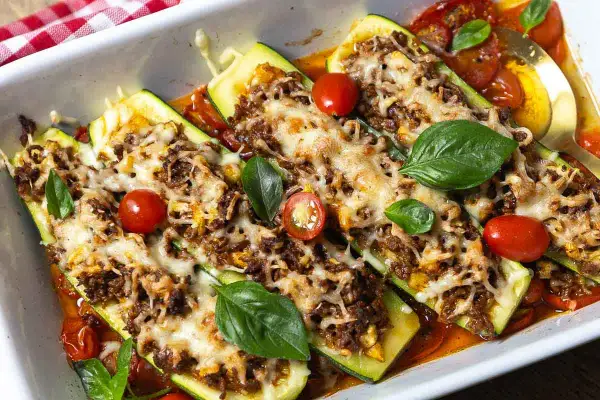 Herzhafte zucchini schiffchen mit Hackfleisch und Käse überbacken, garniert mit frischem Basilikum und Kirschtomaten.
