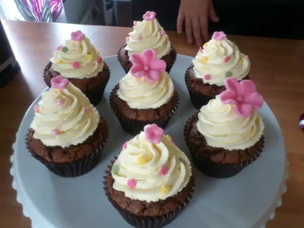 Sju chokladmuffins med fluffig vit choklad frosting, dekorerade med rosa blommor och strössel. Perfekt för ett kalas!