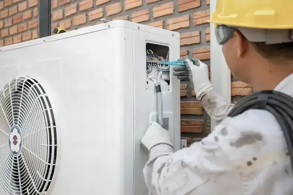 Technik w żółtym kasku reguluje okablowanie pompy ciepła, co może pomóc w optymalizacji jej pracy, np. jak zmniejszyć taktowanie pompy ciepła.