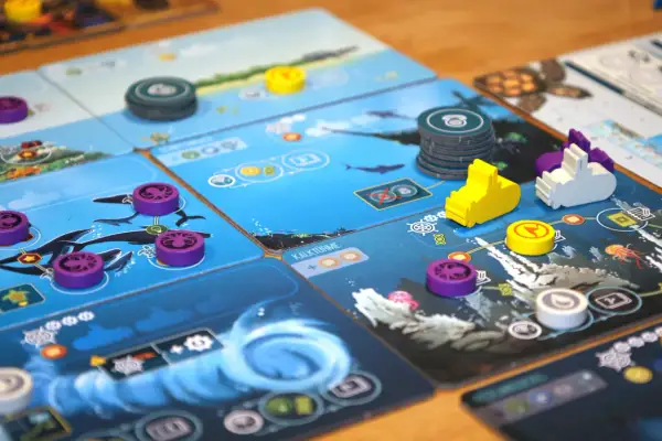 Ein komplexes Brettspiel mit Meeresmotiven. Lila und gelbe Spielsteine auf blauen Karten mit Walen und Quallen. Ein Kennerspiel, das strategisches Denken erfordert.