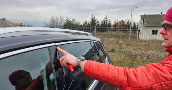 Mężczyzna w czerwonej kurtce wskazuje palcem na drzwi swojego pierwszego samochodu, trzymając w dłoni czerwony przyrząd.