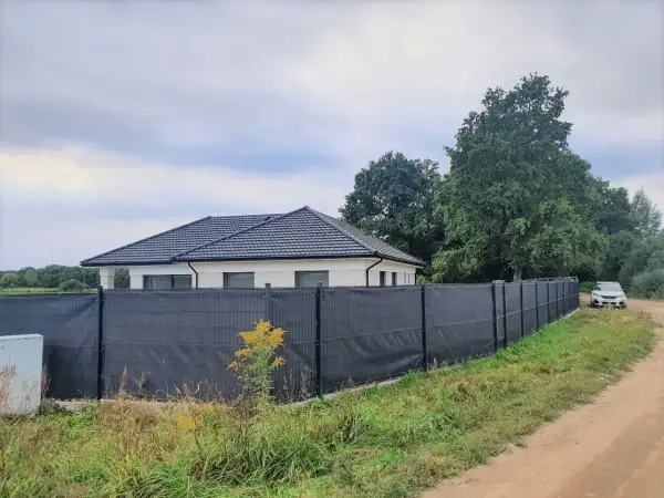 Nowoczesna siatka ogrodzeniowa skutecznie zasłania płot, zapewniając prywatność. Dom i samochód w tle.