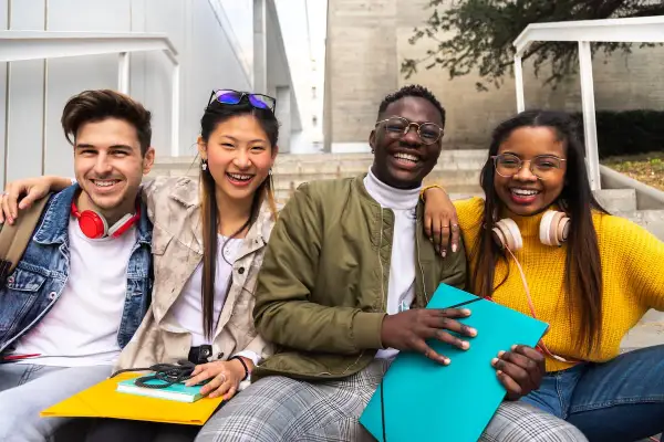 Cuatro jóvenes sonríen sentados en escaleras, planeando su futuro, quizás para trabajar en el extranjero.