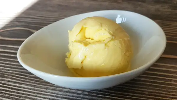 Cremiges Mango-Eis, selbst gemacht mit der Eismaschine, in einer weißen Schale auf Holztisch.