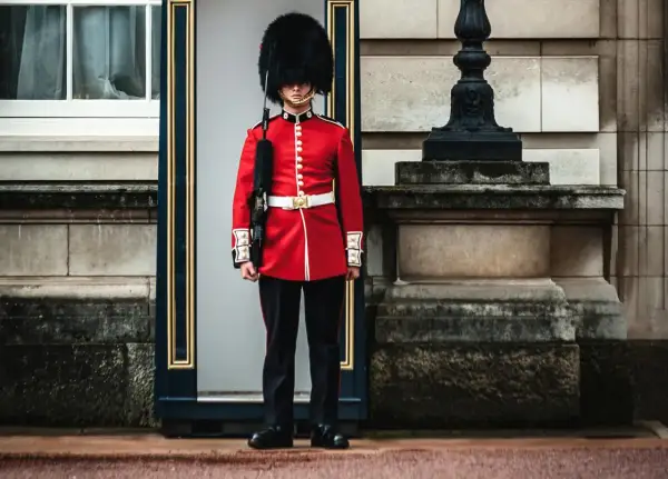 Un guardia con uniforme rojo y sombrero de piel, un típico inglés, vigila la entrada de un edificio histórico.