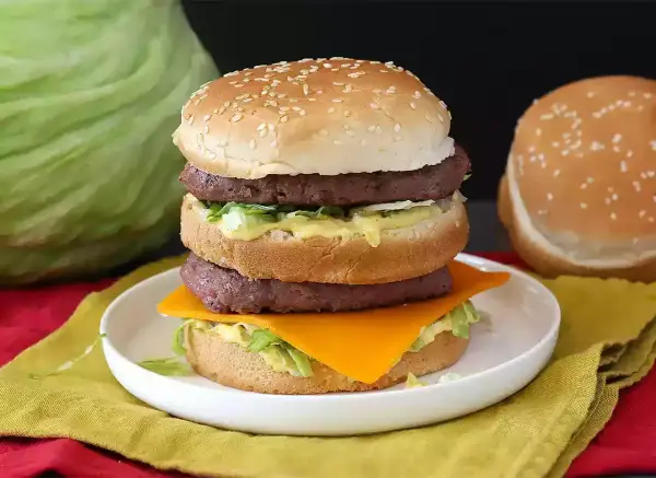 Domowy Big Mac z dwoma kotletami, serem, sałatą i sosem na talerzu.