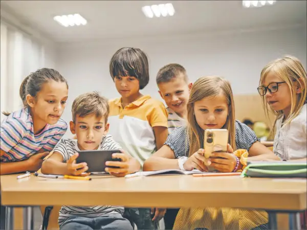 Dzieci skupione na ekranach telefonów i tabletu, uczące się i bawiące razem. Wspólna **socjalizacja** w cyfrowym świecie.