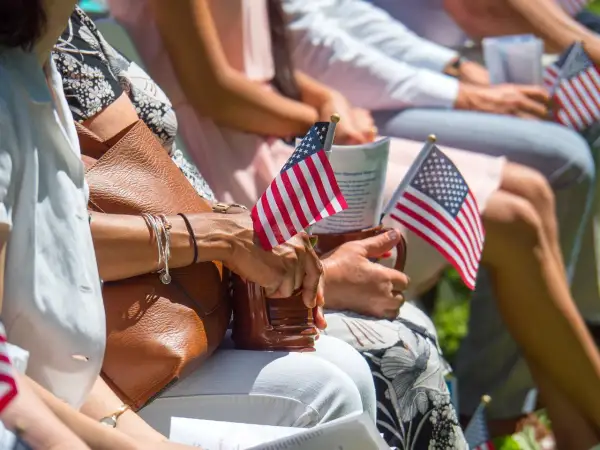 Manos sostienen pequeñas banderas de EE.UU. en un evento, quizás celebrando el sueño de estudiar en Estados Unidos siendo español.